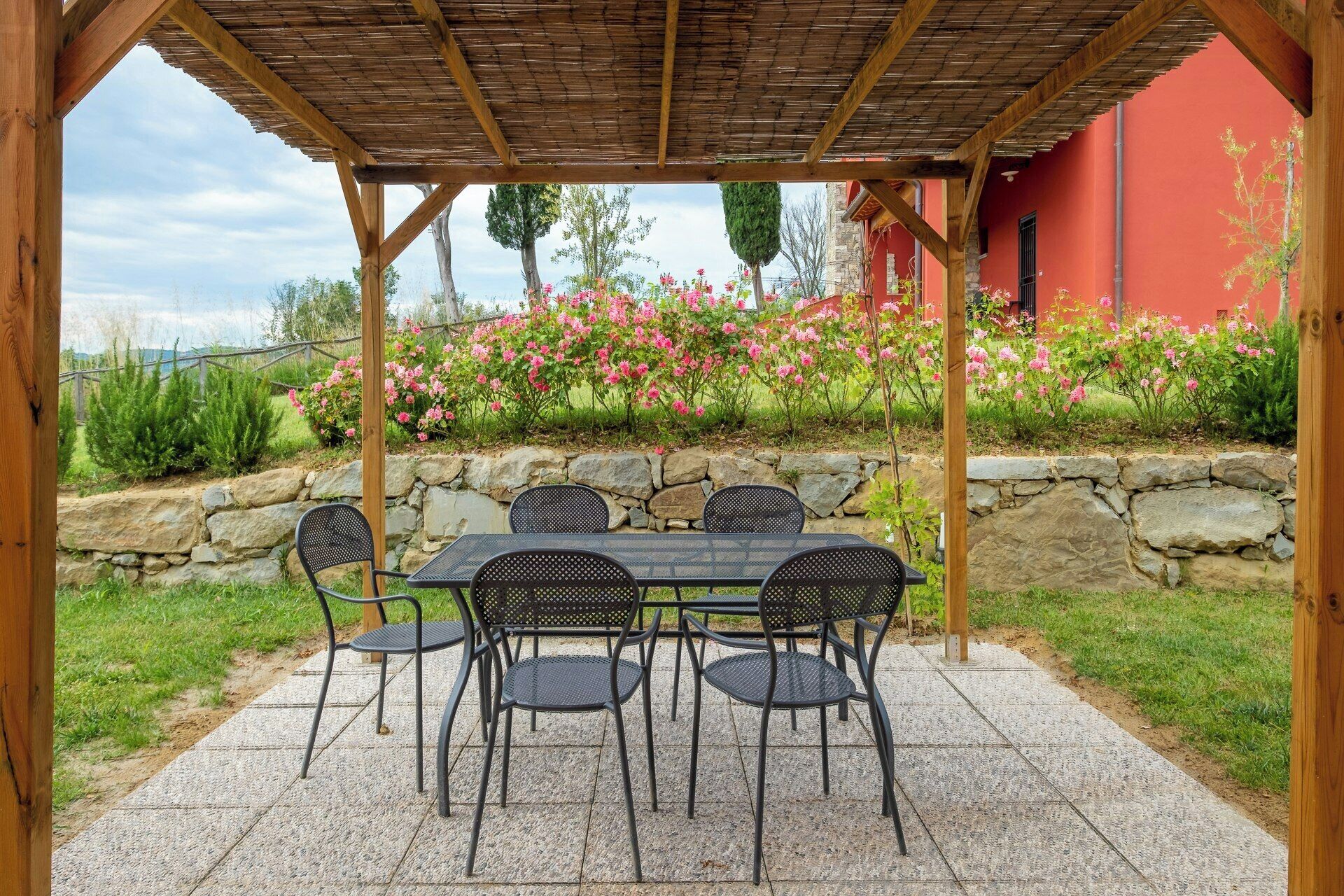 An outdoor patio with a table and chairs, a stone wall, and flowering plants.