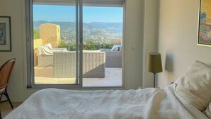 A bedroom with a large sliding glass door leading to a balcony with a wicker sofa and a view of a cityscape. - Sea view villa in Théoule-sur-Mer (Théoule-sur-Mer)
