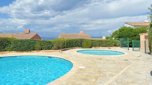 A pool area with two pools, a clear sky, and buildings with red-tiled roofs. - Sea view villa in Théoule-sur-Mer (Théoule-sur-Mer)