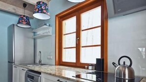 Une cuisine avec des meubles de rangement en bois, une bouilloire en acier inoxydable et une fenêtre avec un cadre en bois.