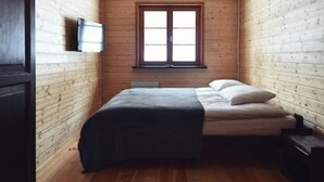 Une petite pièce chaleureuse avec un plafond en bois, un lit recouvert d’une couverture de couleur sombre, une fenêtre donnant sur un beau paysage et un téléviseur fixé au mur.
