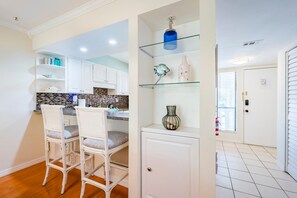 A kitchen with white cabinets, a tiled backsplash, and a bar area with two white wicker chairs. - Secluded Beach Condo w/ Resort Access (Bradenton Beach)