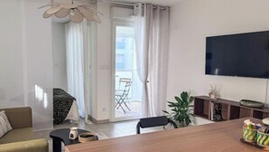 A modern living room with a sofa, a dining table, a TV, and a sliding glass door leading to an outdoor area. - New studio with terrace Airbus Aéroport (Colomiers)
