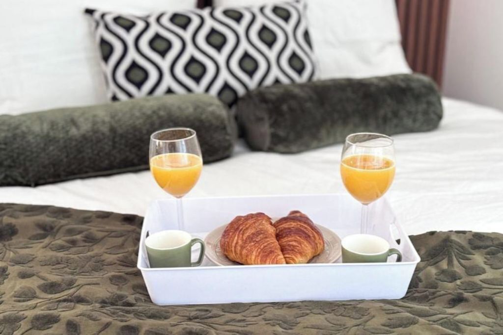 Een bed met twee kussens, een dienblad met croissants, glaasjes sap en kopjes.