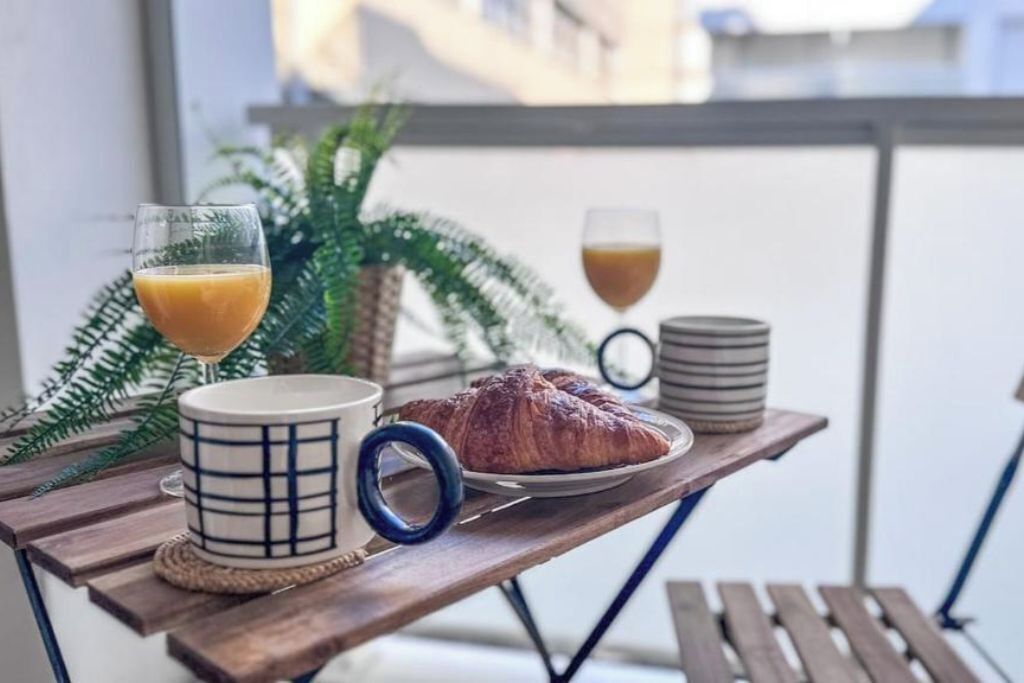 Une table en bois dressée pour le petit-déjeuner, avec un croissant, deux verres de jus d’orange et une tasse.