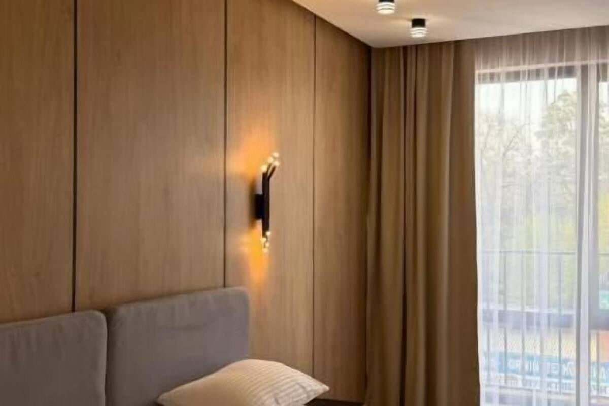 Un dormitorio con una cama grande, paneles de madera en las paredes, una lámpara de pared y una ventana con cortinas.