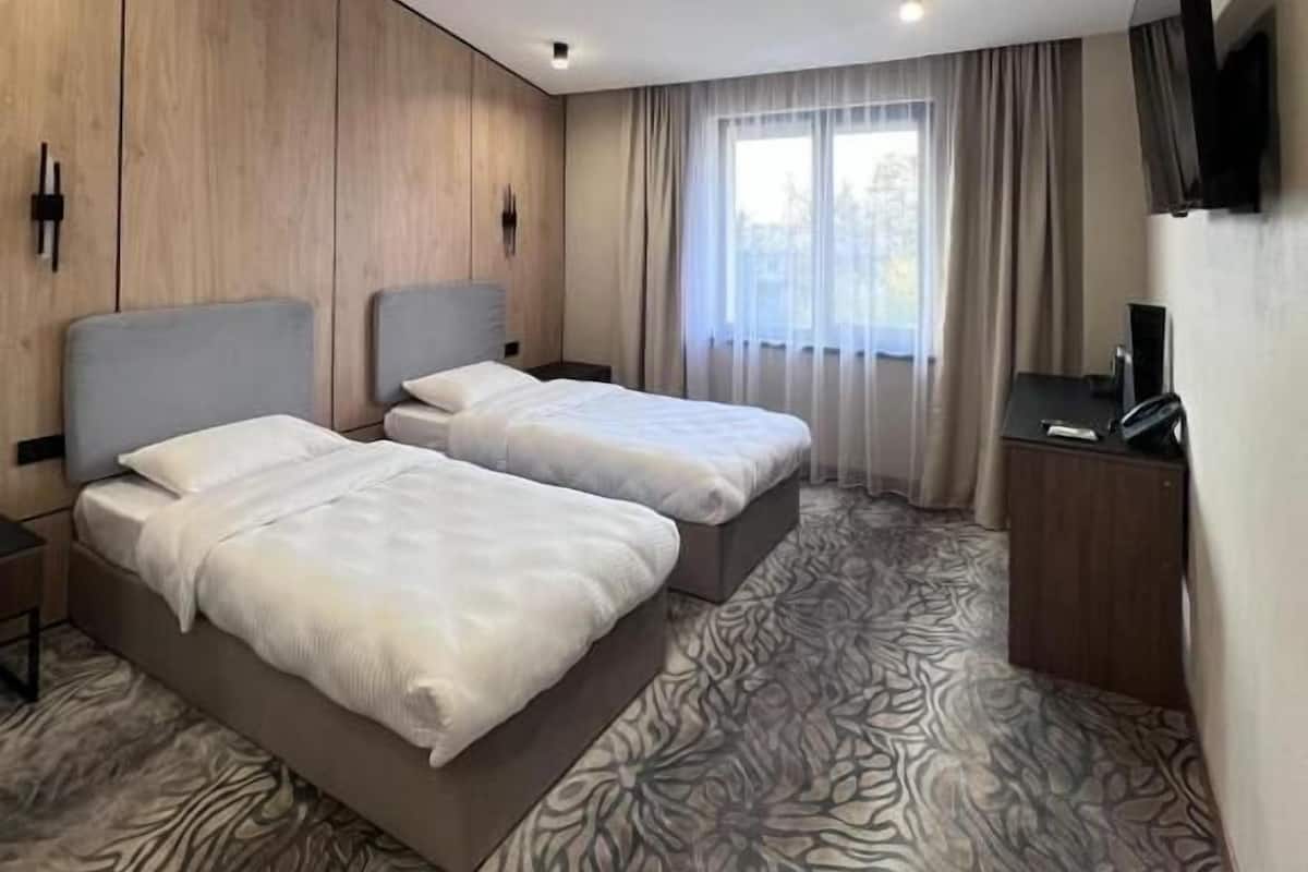 Habitación de hotel con dos camas, un escritorio, un televisor y una ventana con cortinas.