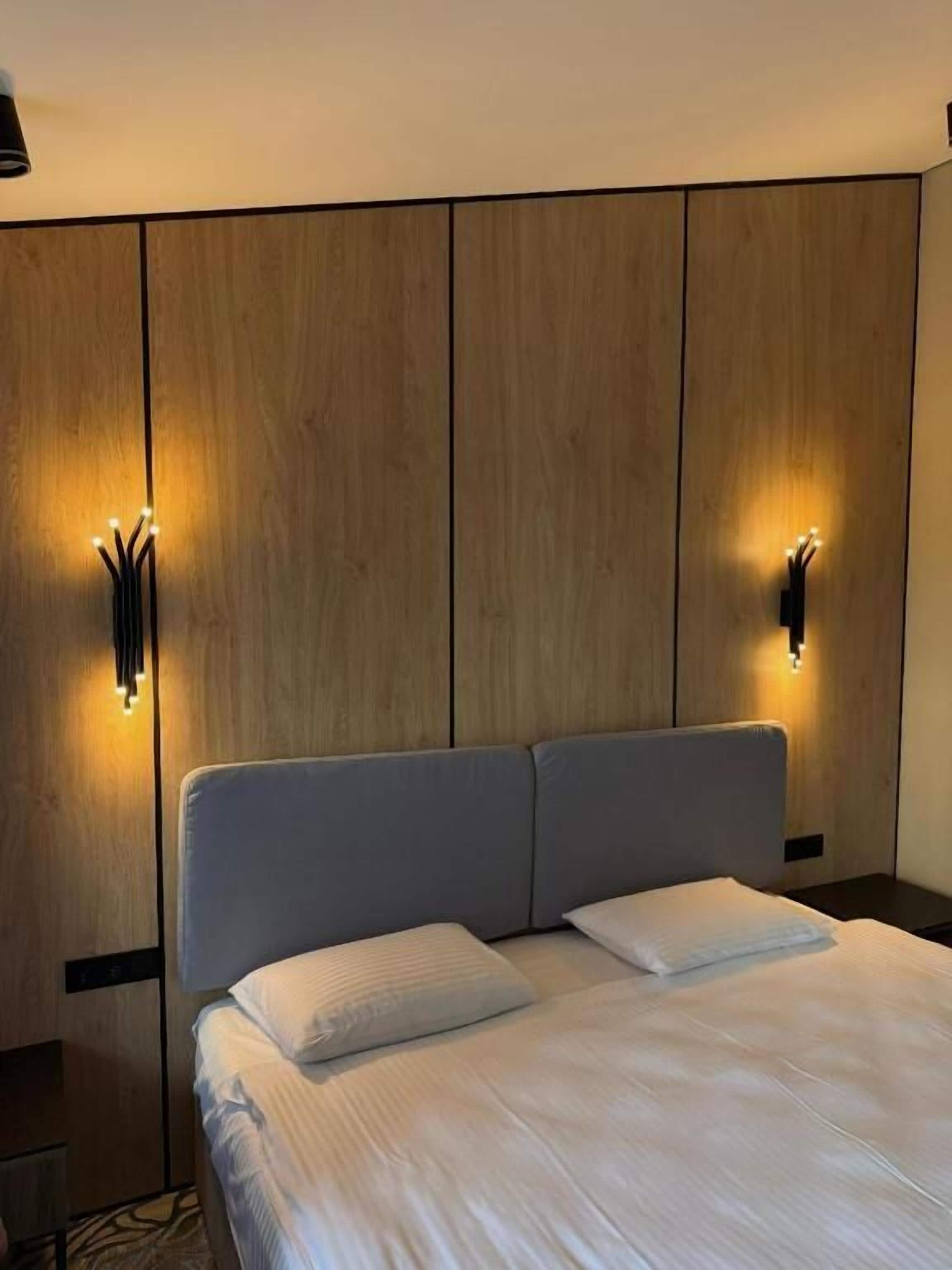 Een moderne hotelkamer met een groot bed, houten paneelwanden en wandlampen.
