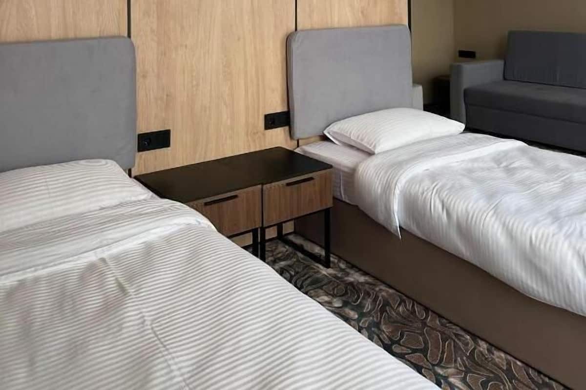 Habitación de hotel con dos camas, un armario de madera, una mesita pequeña y un sofá gris.