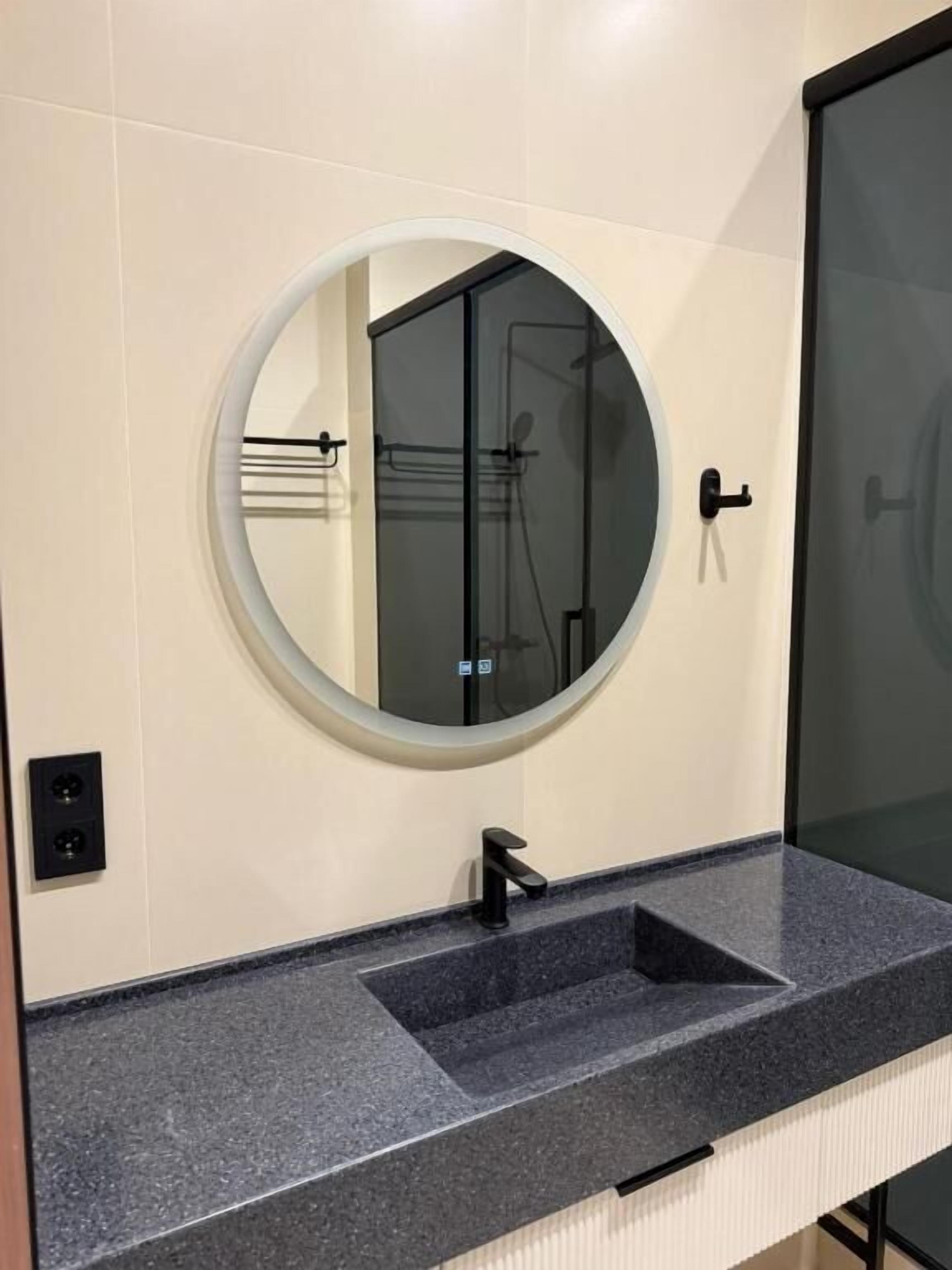 Une salle de bain avec un miroir rond, un lavabo noir et une cabine de douche en verre.
