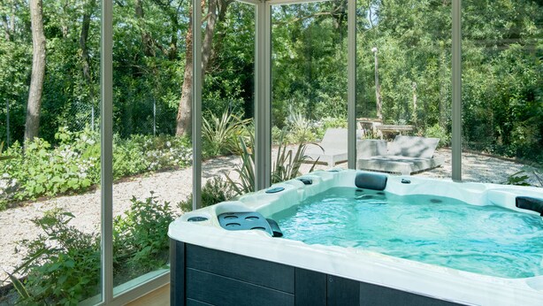 Ein Whirlpool in einem überdachten Außenbereich mit Blick auf einen Garten und Bäume.