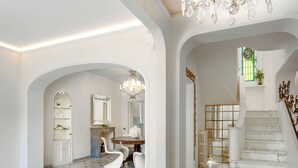 Eine prachtvolle Eingangshalle mit Marmorboden, einem Chandelier, einer Treppe und einem Essbereich mit Tisch und Stühlen.