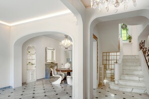 Eine prachtvolle Eingangshalle mit Marmorboden, einem Chandelier, einer Treppe und einem Essbereich mit Tisch und Stühlen.