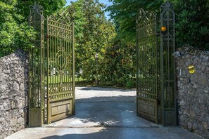 Ein schmiedeeisernes Tor mit aufwendigen Verzierungen, das zu einem gepflasterten Weg führt.