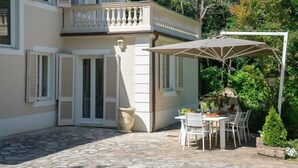 Ein zweistöckiges Gebäude mit einem Balkon, einer Terrasse mit Tisch und Stühlen und einem großen Topf mit Pflanze.