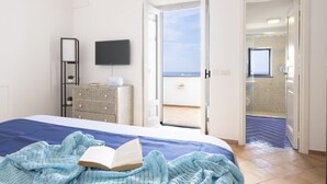 Een slaapkamer met een bed, een boek, een televisie, een dressoir en een balkon met uitzicht.