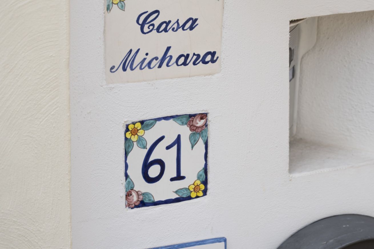 Seinässä on kyltti, jossa lukee ”Casa Michara”, ja sen vieressä on numero ”61”, ja molempia koristavat kukkakuviot.