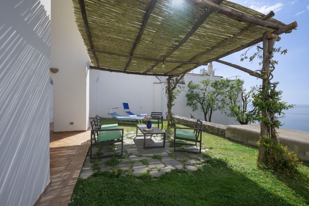 Een terras met een tafel en stoelen, een pergola en uitzicht op zee.