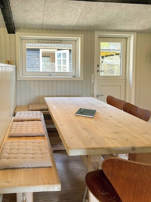 Ein Zimmer mit Holztisch, Bänken und zwei Fenstern.