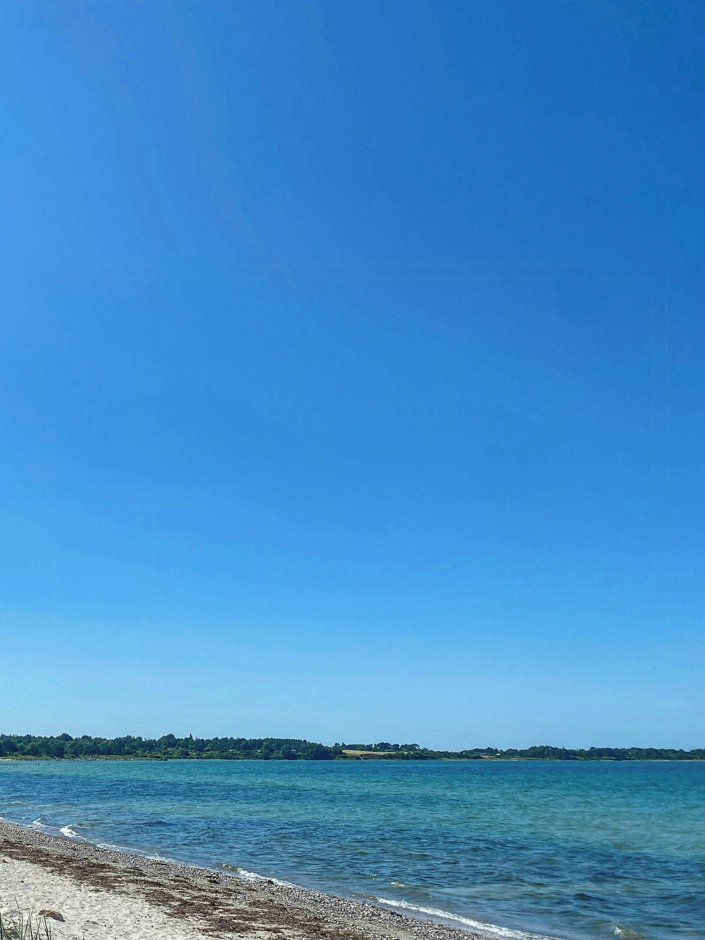 A clear blue sky over a calm body of water with a distant shoreline.