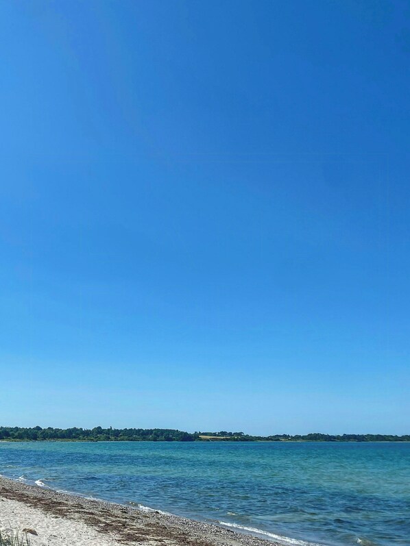 Ein klarer, blauer Himmel über ruhigem Wasser mit einer entfernten Küste.