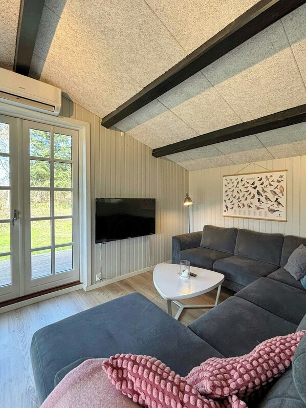 A living room with a large grey sofa, a white coffee table, a flat-screen TV mounted on the wall, and a framed bird illustration.