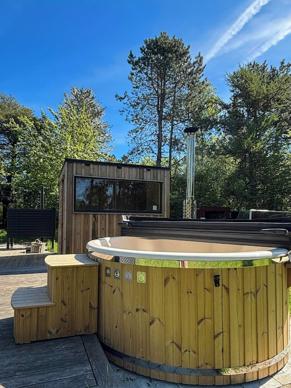 A wooden hot tub with a wooden deck and a small wooden structure with a window.