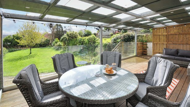 Un patio cubierto con mobiliario de mimbre, una mesa de vidrio y vistas a un jardín verde.