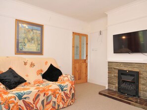 A living room with a sofa, a fireplace, a television, and a door. - Porthmeor (Wadebridge)