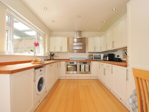 A kitchen with white cabinets, a stainless steel range hood, a microwave, and a washing machine. - Porthmeor (Wadebridge)
