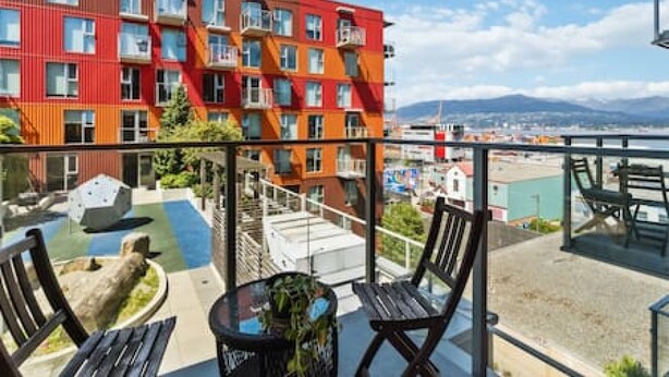 A balcony with a view of a colorful building, outdoor seating, and a clear sky. - Cozy condo with excellent views, 5 mins to arena (Vancouver)