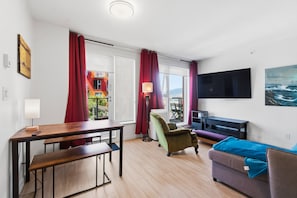 A modern living room with a wooden dining table, a green armchair, a sofa, and a flat-screen TV mounted on the wall.