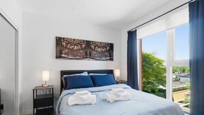 A bedroom with a bed, a nightstand, a lamp, a painting, and a large window with a view. - Cozy condo with excellent views, 5 mins to arena (Vancouver)