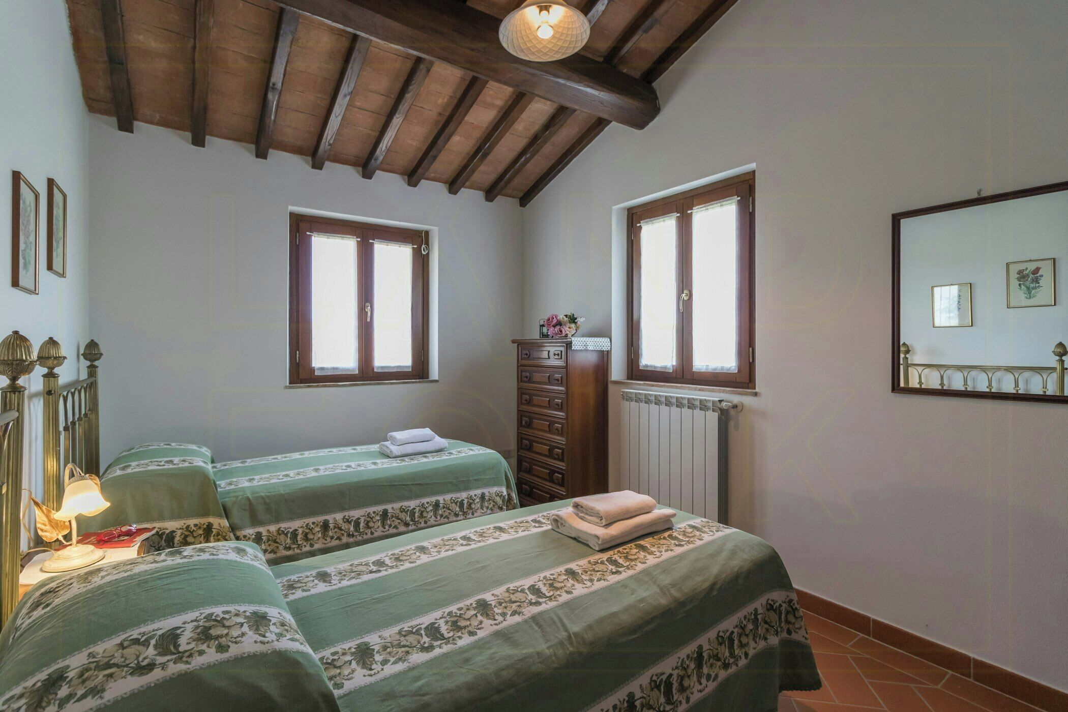 Una stanza con due letti, travi in legno al soffitto, un comò e due finestre.