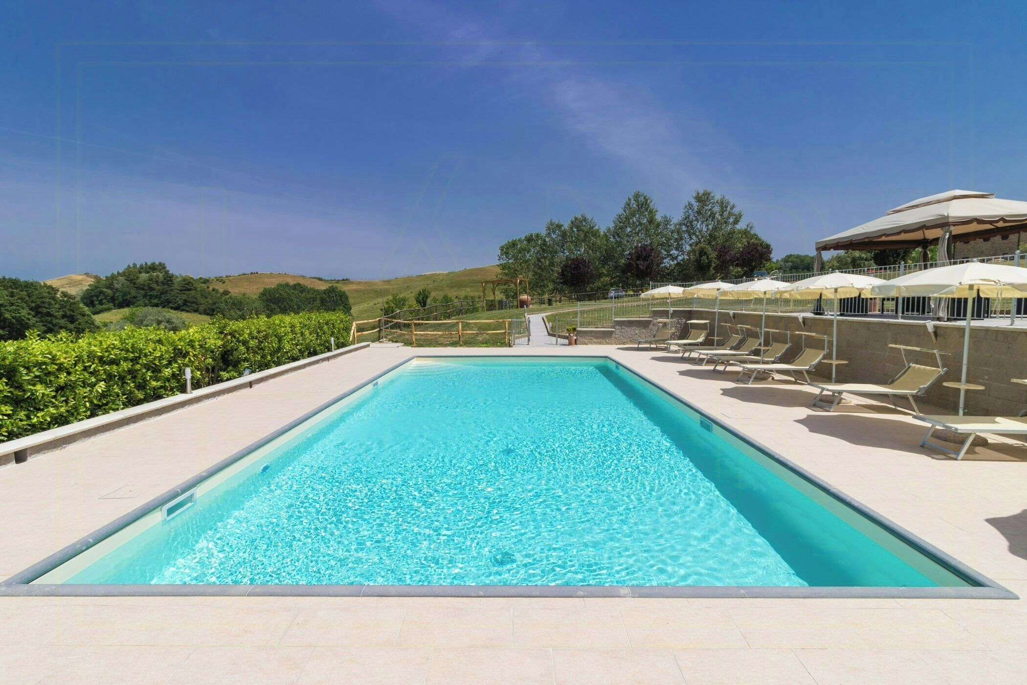 Une piscine rectangulaire à l’eau d’un bleu limpide, entourée d’une terrasse carrelée et de chaises longues.