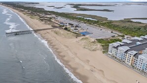 Luchtbeeld van een kustgebied met een strand, een steiger en een hotel met meerdere gebouwen.