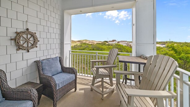 Een balkon met rieten meubels, een tafel en uitzicht op een strand en gebouwen.