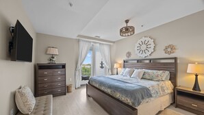 Een slaapkamer met een bed, een dressoir, een bankje, een televisie, een kroonluchter en een raam met gordijnen.