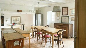 Une cuisine rustique avec une table en bois, des chaises, un réfrigérateur et des luminaires suspendus.