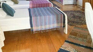 Une chambre confortable située sous les combles, avec des poutres apparentes, deux lits, une table de chevet et une grande fenêtre ornée d’un rideau léger.