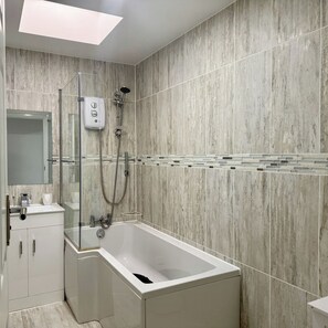 A modern bathroom with a bathtub, shower, and a glass-enclosed shower area. - 4-Bedroom with Double Beds Retreat Modern Elegance (Portsmouth)