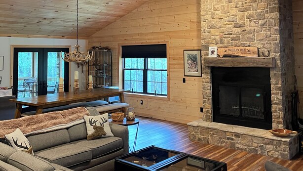 A spacious living room with a stone fireplace, wooden ceiling, and a large sofa. - Welcome to 'Legacy Lodge',' your ultimate Centre County PA cabin getaway! (Munson)