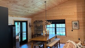 A spacious room with a wooden ceiling, a dining table with benches, a ceiling fan, and a large window. - Welcome to 'Legacy Lodge',' your ultimate Centre County PA cabin getaway! (Munson)