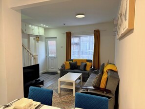 Una sala de estar con un sofá, una mesa de centro, un televisor y una escalera que lleva a otra habitación.