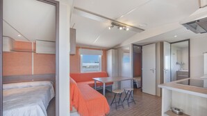 A compact room with a bed, a small table, a bench, and a kitchenette area. - Bungalow 'Tranquilo Cerca De Roche' with Private Pool, Wi-Fi and Air Conditioning (Conil de la Frontera)