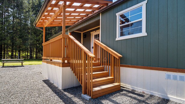 Eine Holztreppe führt zu einer überdachten Veranda mit einer Bank im Hintergrund.
