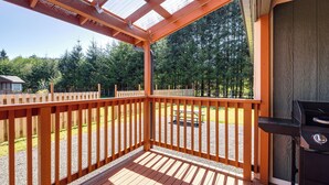 Eine Holzterrasse mit Grill und Picknicktisch, umgeben von einem Zaun und Bäumen.
