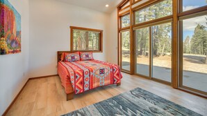 A bedroom with a large window, a bed with patterned bedding, and a painting on the wall.
