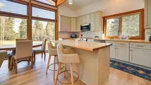 A modern kitchen with a bar area, wooden flooring, and large windows offering a view of trees.