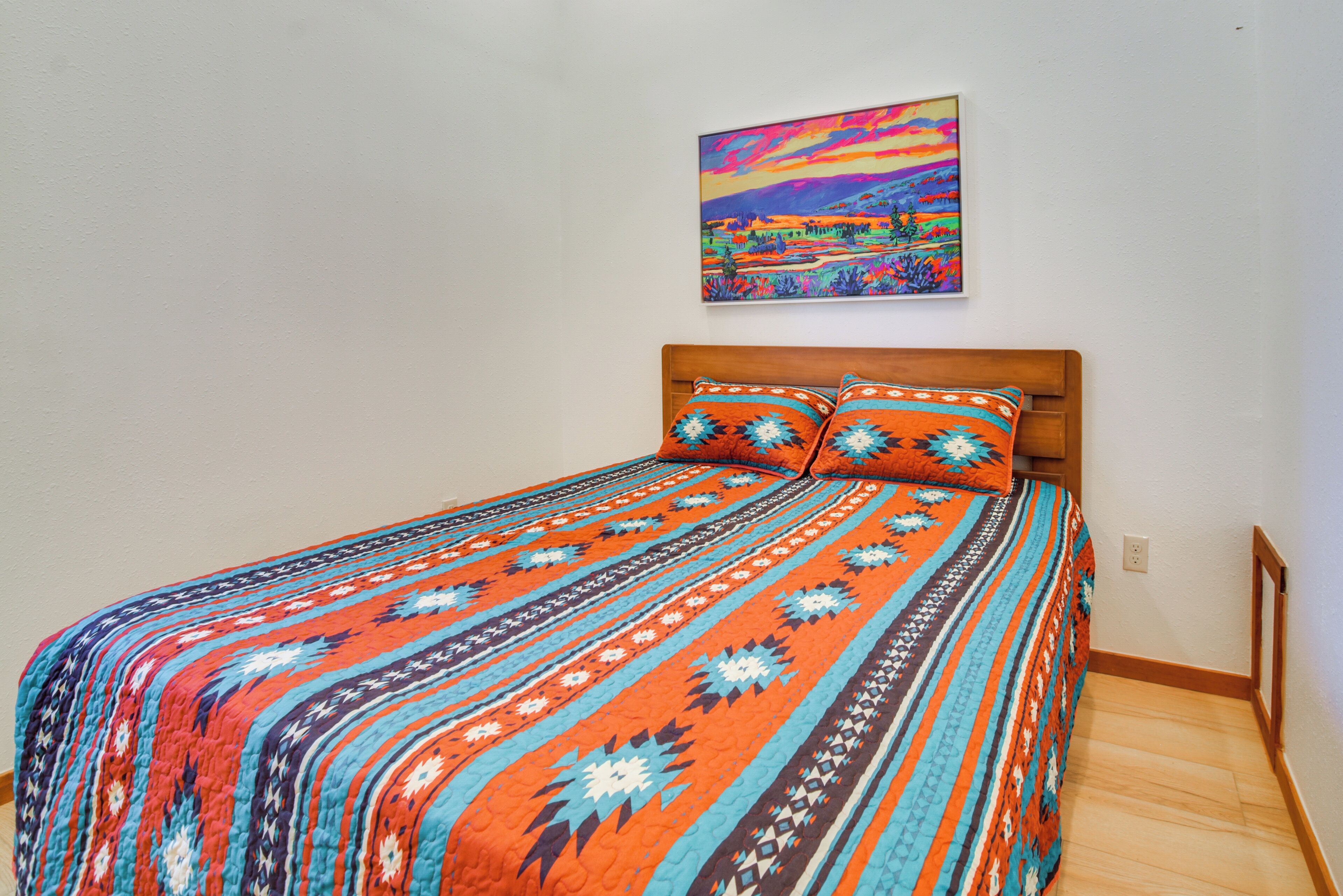 Ein Bett mit einer farbenfrohen Steude, einem Holzkopfteil und einem Bild an der Wand.